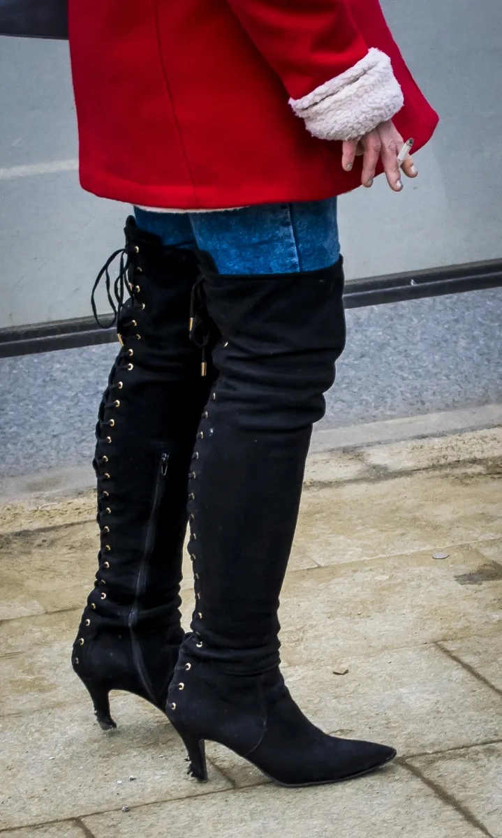 Red coat and black lace-up boots with a cigarette held behind one hand